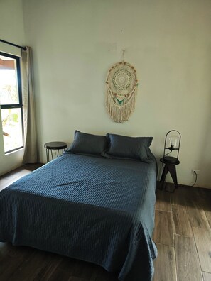 Un dormitorio con una cama, un adorno de pared, una mesita y una lámpara de pie.
