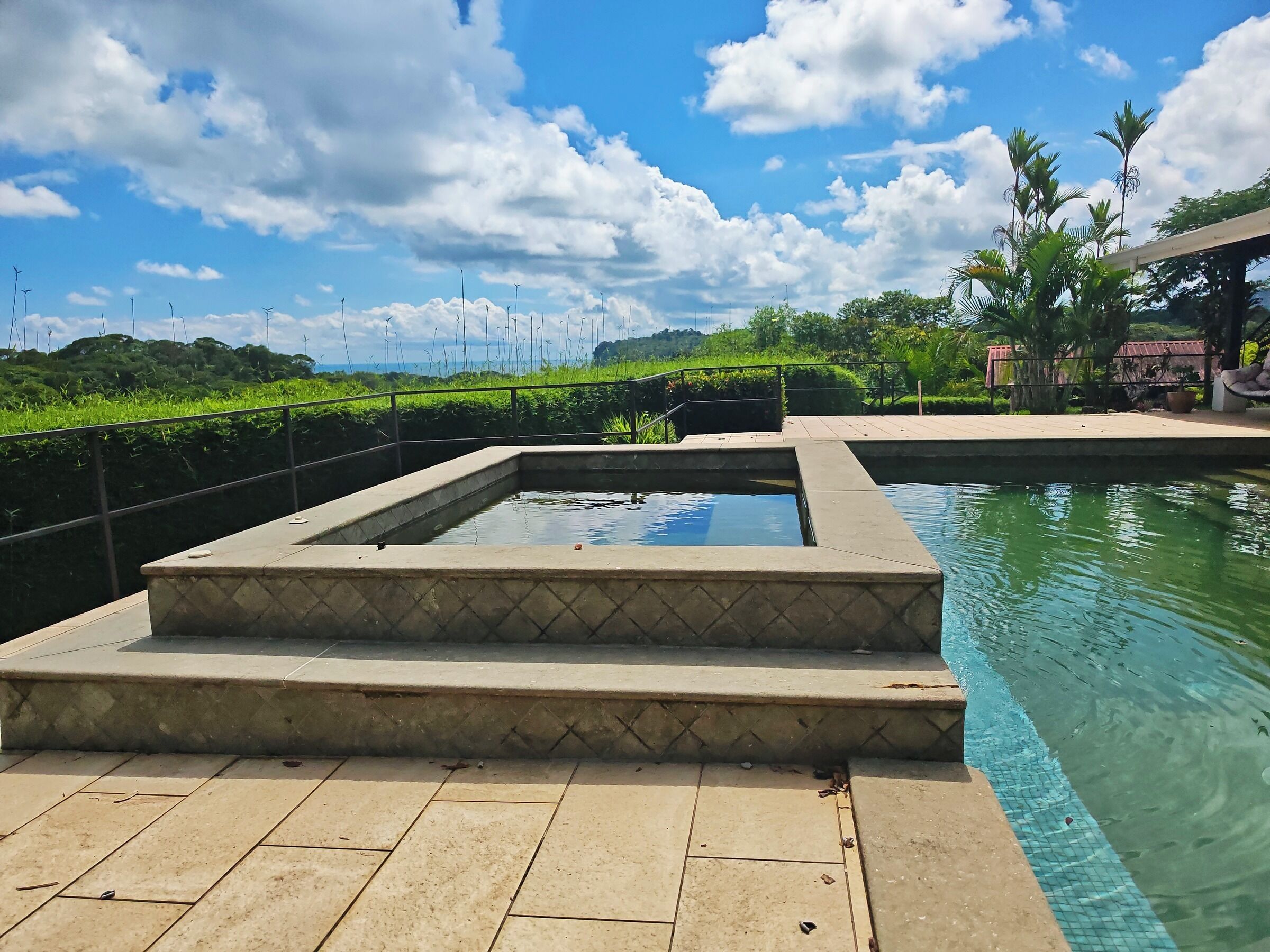 Une piscine dotée d’une terrasse carrelée, entourée de verdure et surplombée par un ciel dégagé.