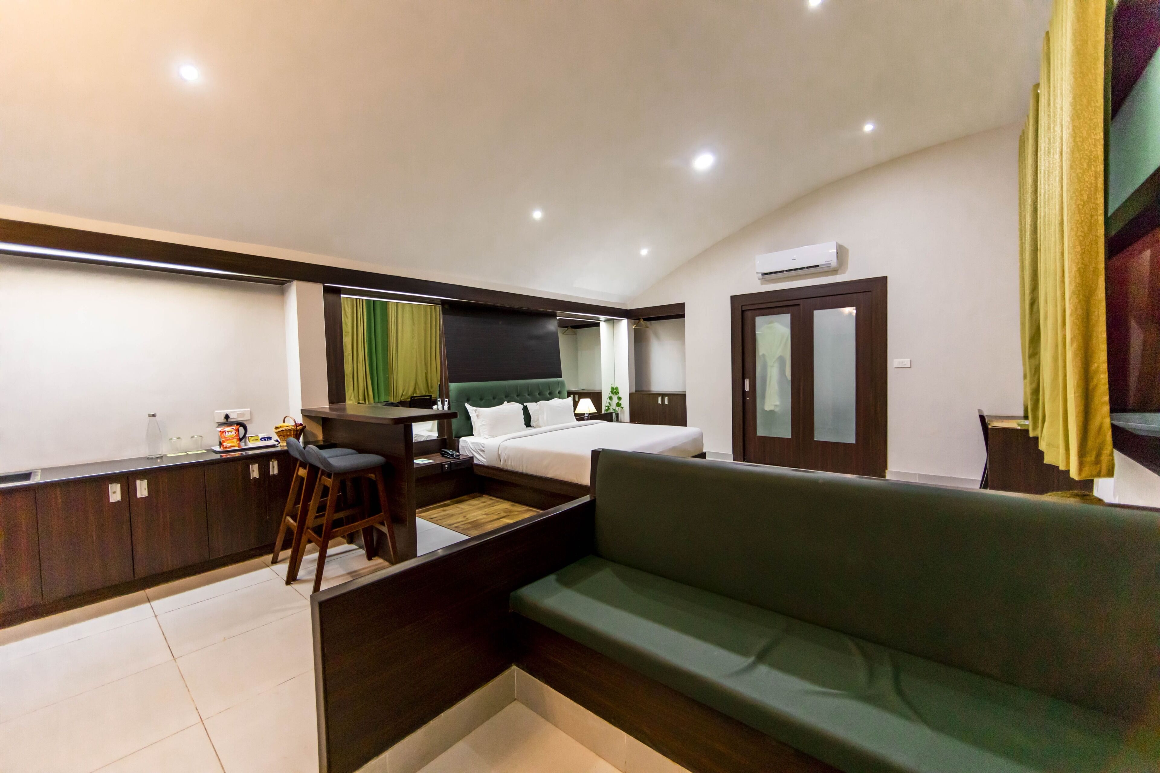 A compact hotel room with a bed, a sofa, a small kitchen area, and a bathroom.
