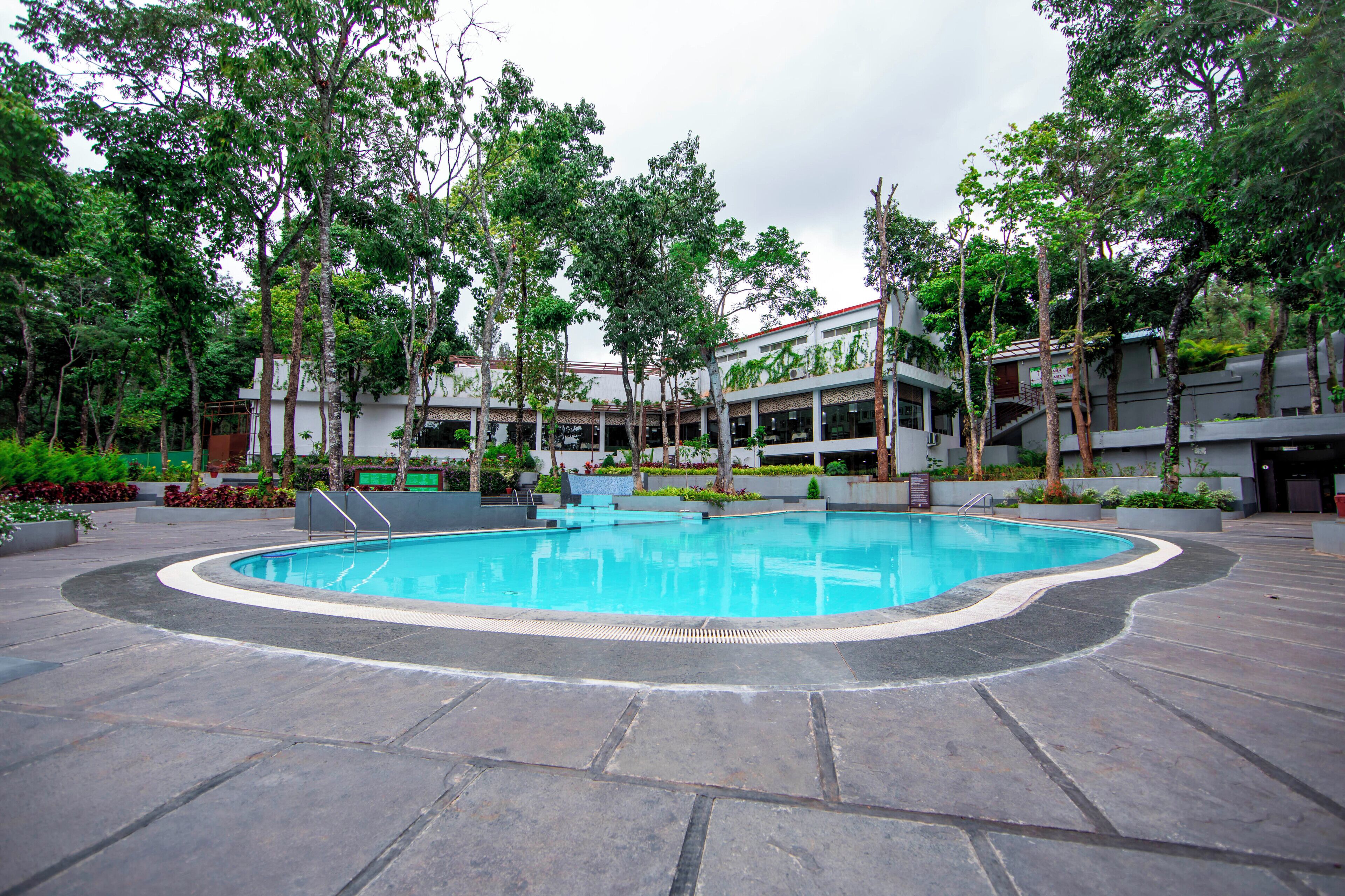 A swimming pool surrounded by trees and a building with a modern design.