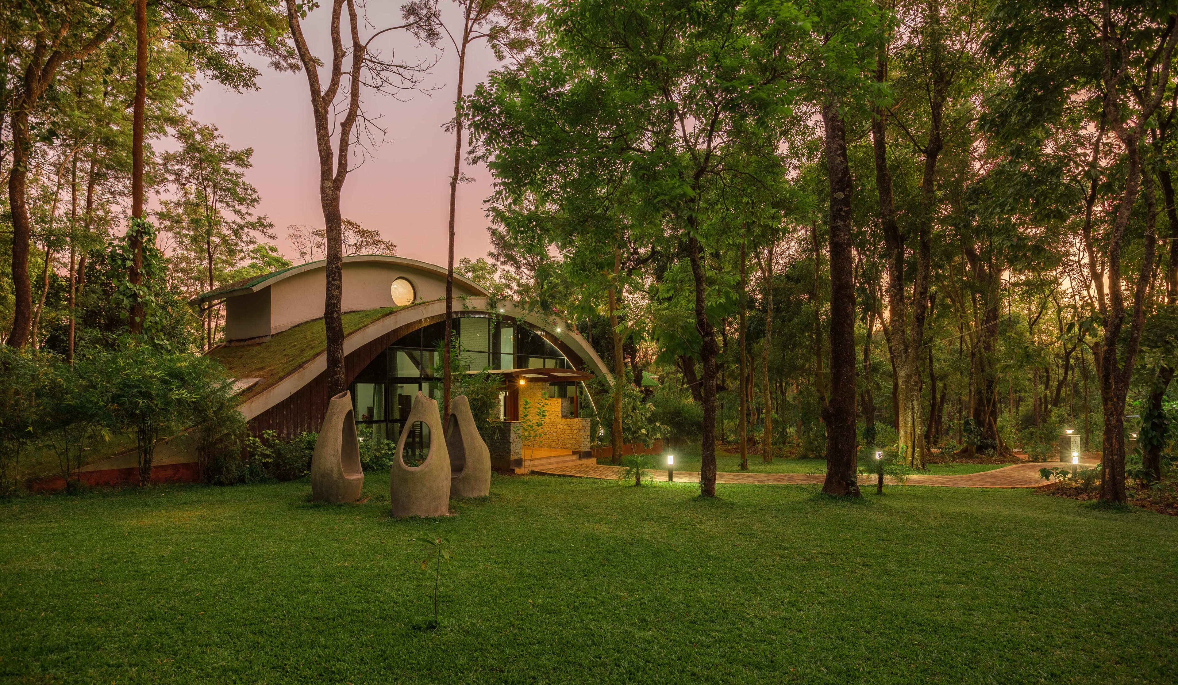 A modern house with a curved roof, surrounded by a lush green lawn and tall trees.
