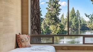 A room with a large window, a bed with a patterned pillow, and a view of a lake and trees. - Riverfront w/dock and big backyard. Enjoy your own slice of the Deschutes River. (Bend)