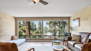 A spacious living room with a large window, a ceiling fan, and a view of a lake and trees. - Riverfront w/dock and big backyard. Enjoy your own slice of the Deschutes River. (Bend)