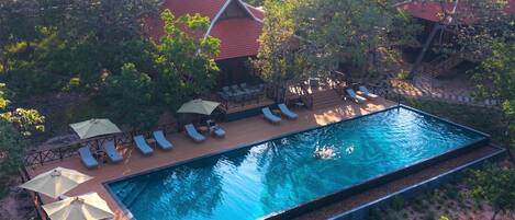 An aerial view of a resort with a swimming pool, lounge chairs, and a small building with a red roof.