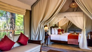 Een slaapkamer met een bed, een bank, een nachtkastje, een lamp en uitzicht op de omgeving.