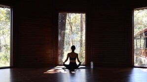 Een kamer met houten wanden, een groot raam en een yogamat op de vloer.