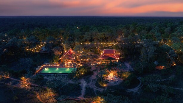 Luchtbeeld van een resort met twee hoofdgebouwen, een zwembad en omliggend groen.