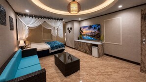 Une chambre d’hôtel avec un lit, un canapé, une table basse, une télévision et un tableau représentant une scène de plage.
