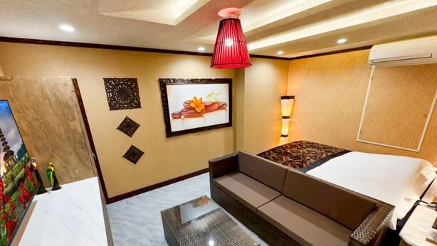 Habitación de hotel con cama, sofá, una mesita, televisor montado en la pared y una lámpara colgante roja.