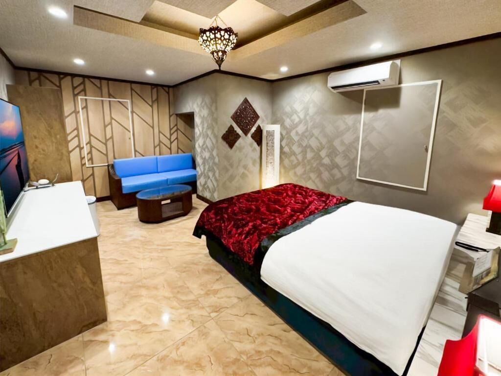 Une chambre d’hôtel moderne avec un lit, un canapé bleu, un bureau et un lustre.