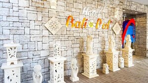 Un mur de pierre sur lequel est apposée une enseigne indiquant « Hôtel Bali Bali », ainsi que des statues blanches décoratives.