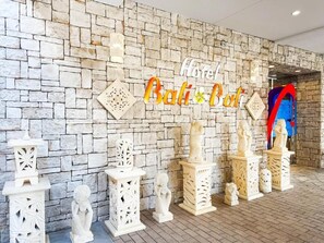 Um muro de pedra com uma placa indicando 'Hotel Bali Bali' e estátuas brancas decorativas.