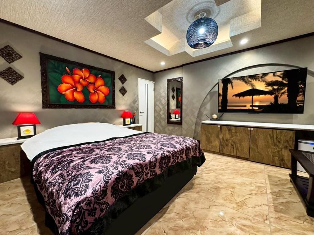 A bedroom with a bed, a vanity with a mirror, a wall-mounted TV, and a ceiling light fixture.