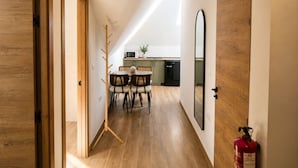 A narrow hallway with a wooden floor, a dining area with a table and chairs, a kitchen with appliances, and a fire extinguisher. - Madrid Pad With 2 Baths (Madrid)
