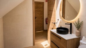 A modern bathroom with a wooden vanity, a round mirror with integrated lighting, and a visible fire extinguisher. - Madrid Pad With 2 Baths (Madrid)