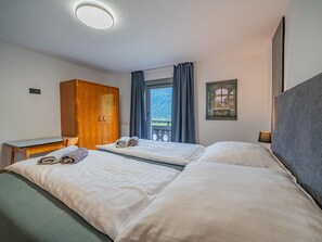 A hotel room with two beds, a wooden wardrobe, a desk, and a window with a view of a balcony.