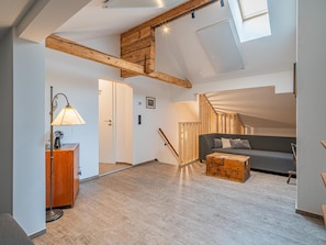 Un loft espacioso con techos altos, vigas de madera a la vista, una escalera, un sofá, una mesa de centro y un escritorio con una lámpara.