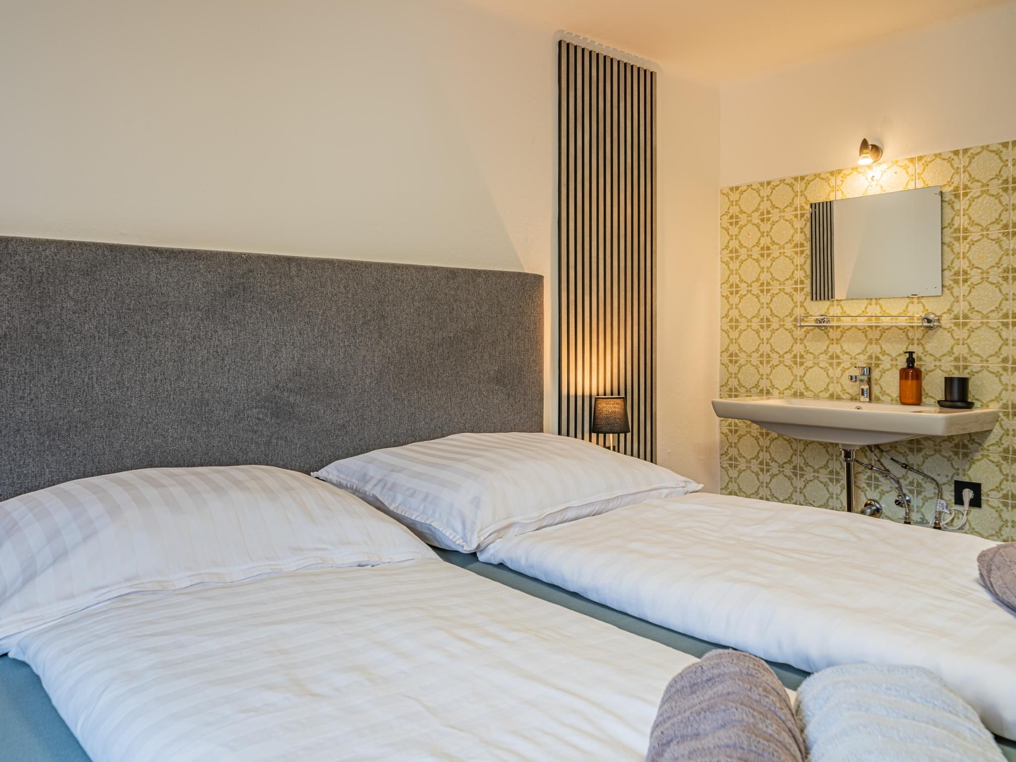 A hotel room with two beds, a vertical light fixture, a wall-mounted sink, and patterned wallpaper.