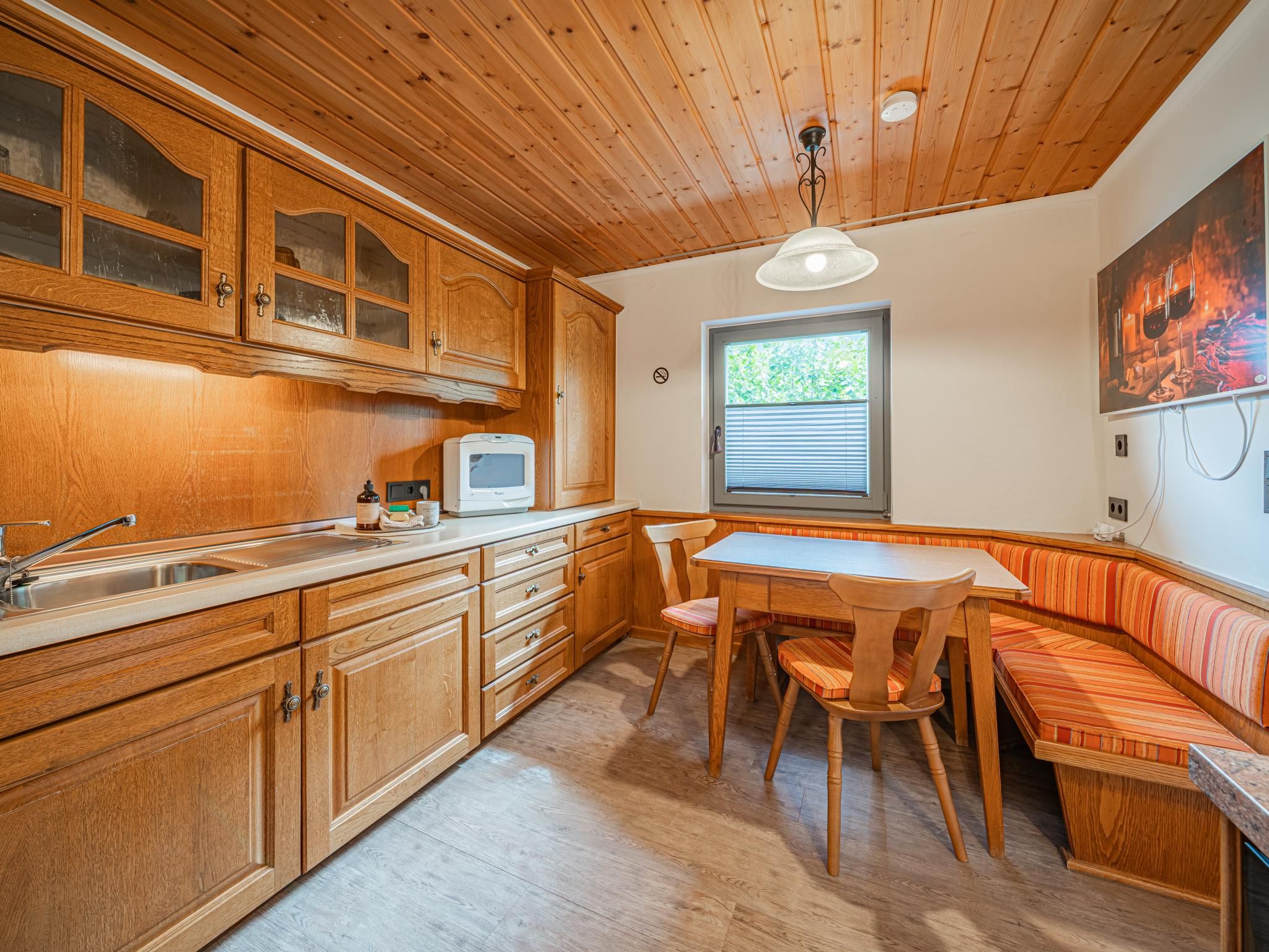 A kitchen with wooden cabinets, a microwave, a sink, and a dining area with a bench.