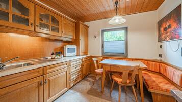 A kitchen with wooden cabinets, a microwave, a sink, and a dining area with a bench.