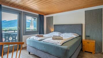 A bedroom with a large bed, a view of a church through a window, and a balcony with a view of the countryside.