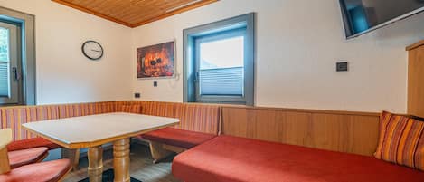 A room with a wooden ceiling, a table with chairs, a bench, and a television mounted on the wall.