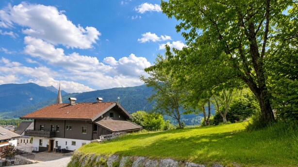 A traditional chalet with a sloped roof, a stone wall, and a gravel path leading to the entrance.