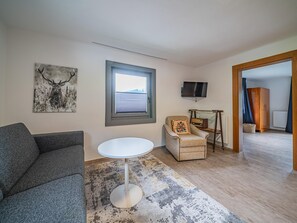 A living room with a grey sofa, a round white table, a patterned rug, a television, and a painting of a deer.