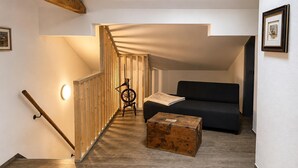 A modern interior with a wooden staircase, a black sofa, a wooden chest, and a spinning wheel.