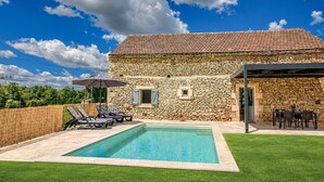 Una casa de piedra con piscina, mobiliario de exterior y un porche cubierto.