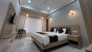 A modern bedroom with a bed, bedside table, chair, ceiling fan, and wall-mounted TV. - The Hotel Phoenix Inn (Indore)
