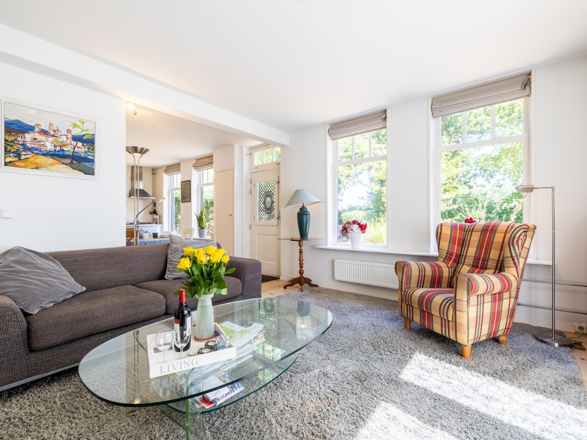 A living room with a sofa, armchair, glass coffee table, and a painting on the wall.