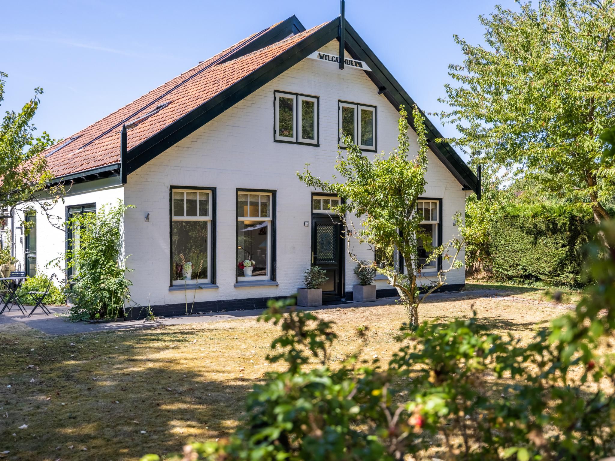 A two-story white building with a red-tiled roof, multiple windows, and a small garden area with potted plants.