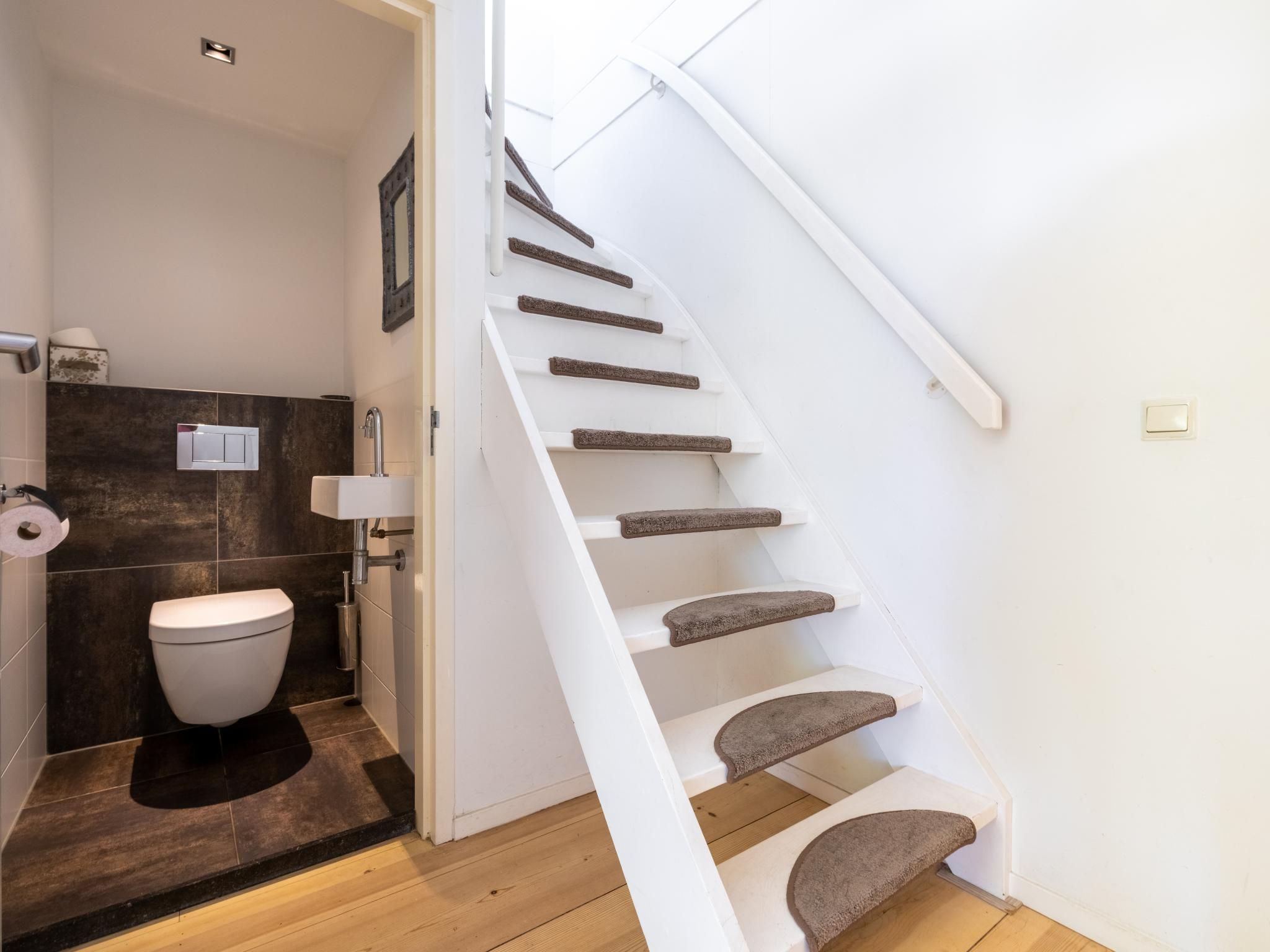 Un baño moderno con inodoro, lavamanos y una escalera blanca con escalones alfombrados.