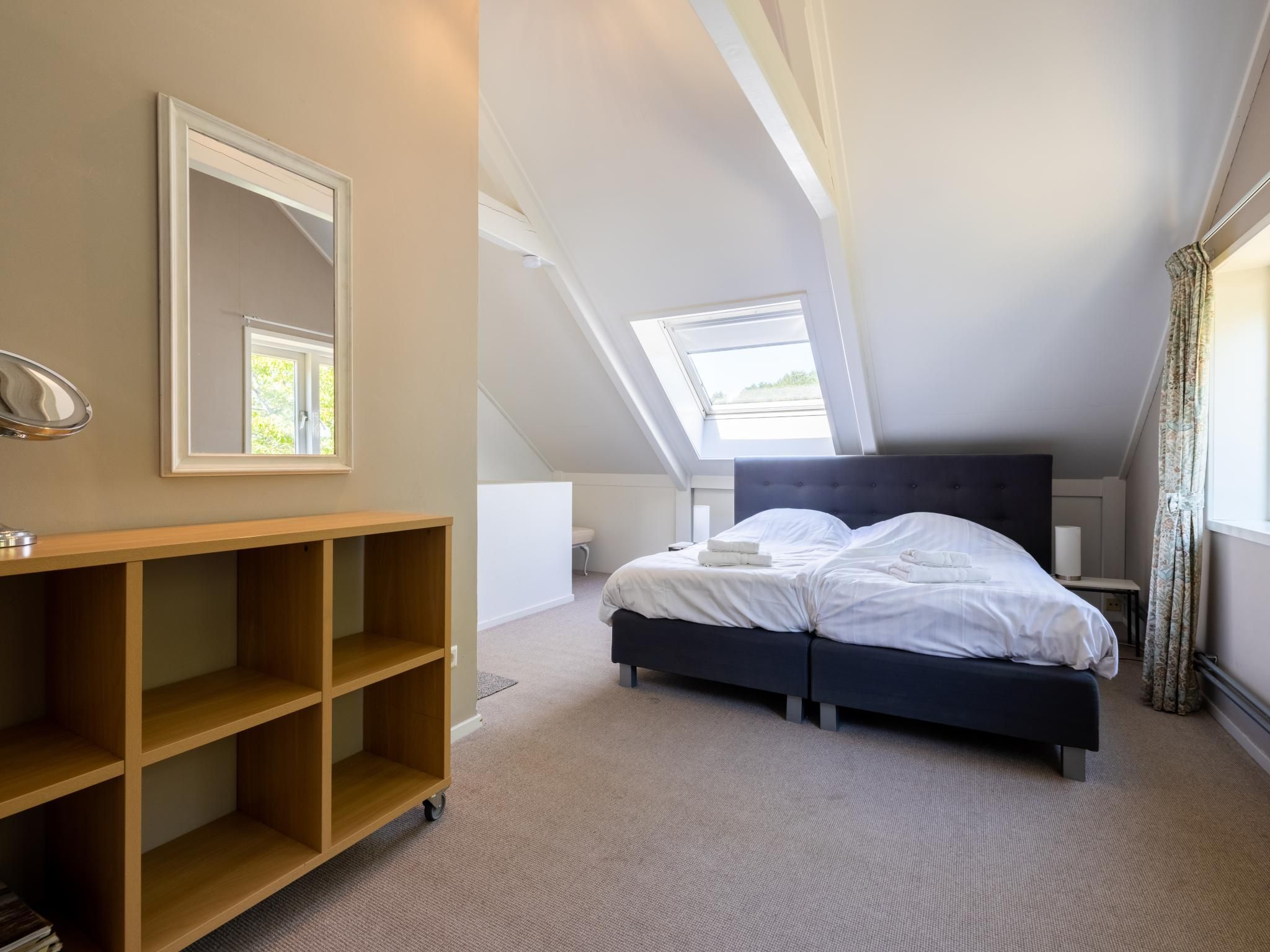 A bedroom with a bed, a wooden shelf, a mirror, and a skylight.