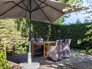 Eine Terrasse im Freien mit Tisch und Stühlen, einem großen Sonnenschirm und einem Kiesgrund.