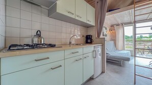 Eine kompakte Küche mit Gasherd, Wasserkocher und Kaffeemaschine, angrenzend an ein Bett mit Blick ins Freie.