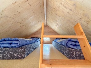 A small, cozy attic room with a sloped ceiling, two single beds with patterned bedding, and a wooden ladder. - Detached beach house, quiet location (Ellemeet)