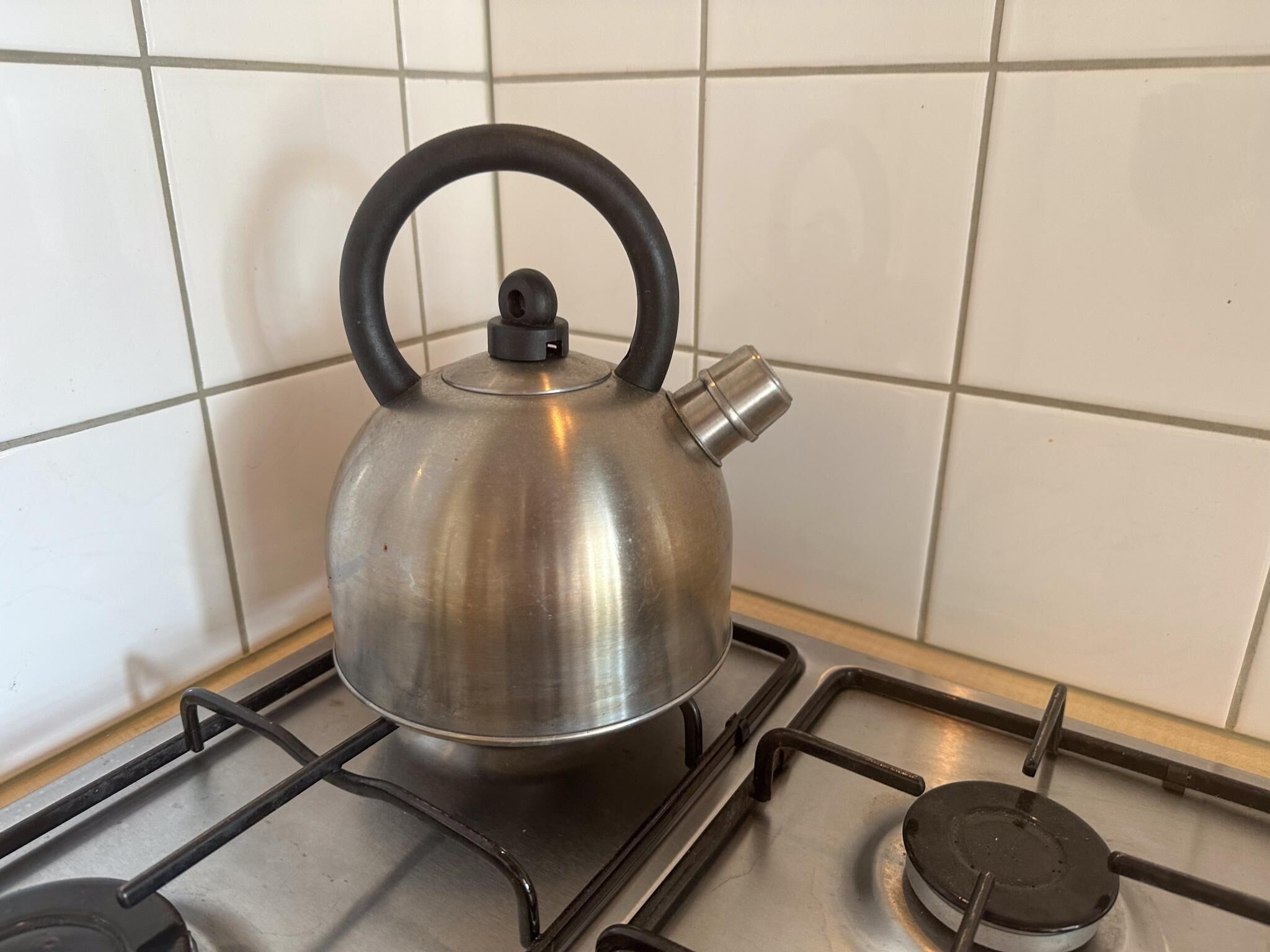 A stainless steel kettle on a gas stove with a black handle.