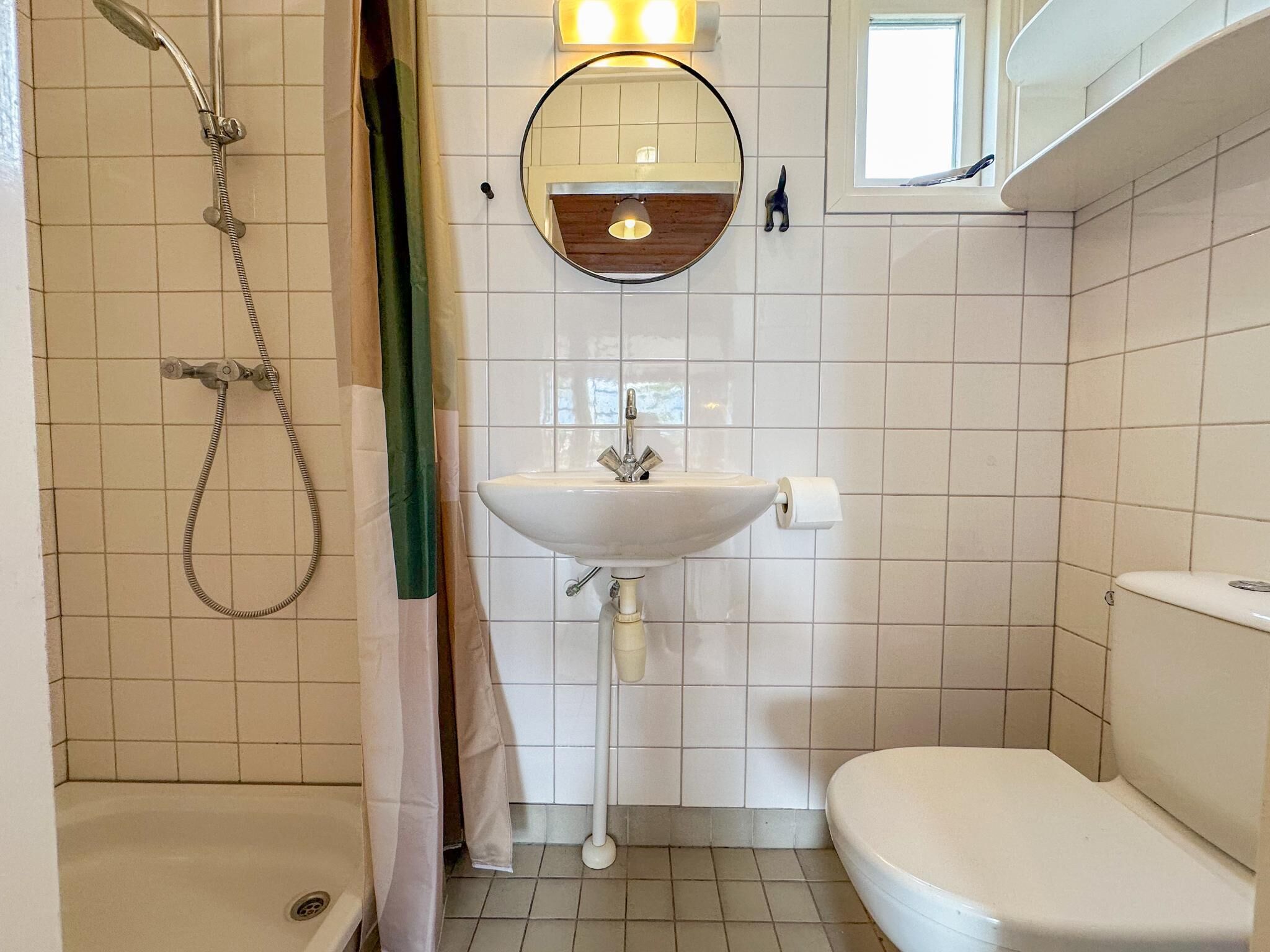 Een badkamer met douche, wastafel, toilet en spiegel met lamp erboven.