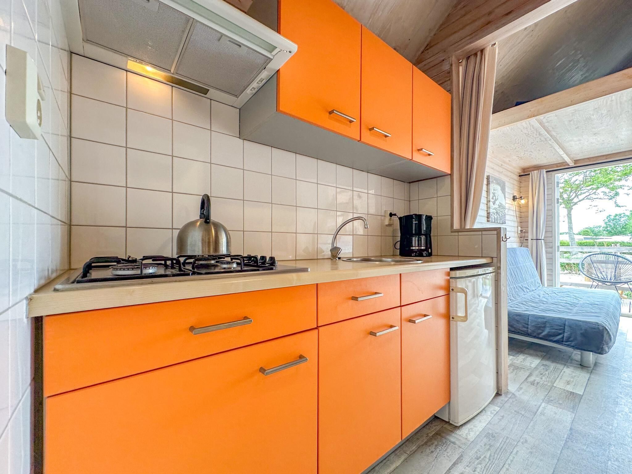 Een kleine keuken met oranje kastjes, een gasfornuis, een waterkoker, een koffiezetapparaat en een spoelbak.