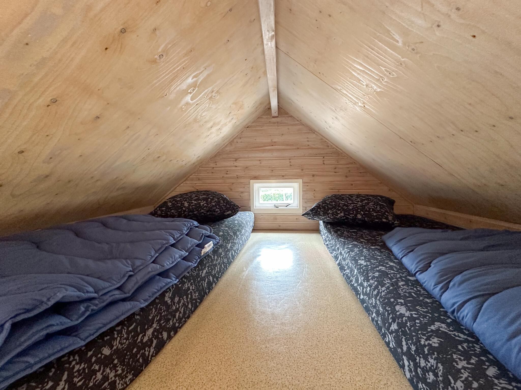 Une petite chambre mansardée, chaleureuse et accueillante, avec deux lits, un plafond en bois et un tableau encadré au mur.