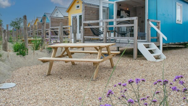 A blue house with a wooden deck and a picnic table. - Peacefully located beach house for families (Ellemeet)
