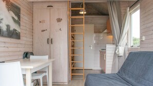 A compact room with a sofa, a dining table with chairs, a ladder, and a kitchenette. - Peacefully located beach house for families (Ellemeet)