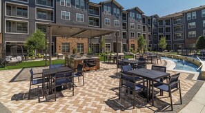 A multi-story building with outdoor seating areas, a barbecue, and a swimming pool. - Elegant 1-bedroom apartment in charming Frisco with rooftop pool and gym (Frisco)