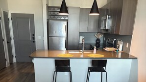 Et moderne køkken med en central ø, to barstole, hængende lamper og en måtte med marmorering.