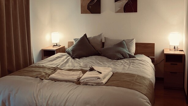 Un letto rifatto con cuscini, un comodino con una lampada e due elementi decorativi appesi al muro.