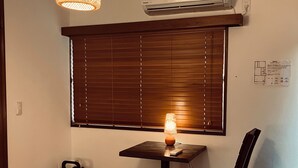 Una stanza con tavolo, sedia, lampadario, condizionatore, persiane e estintore.