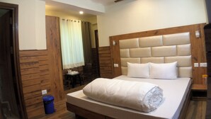A bedroom with a wooden headboard, a bed with white bedding, a blue trash bin, and a wooden floor. - Backwoods B&B Mall Road Shimla (Shimla)