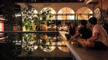 An indoor dining area with a reflective pool, seating arrangements, and a covered roof structure.